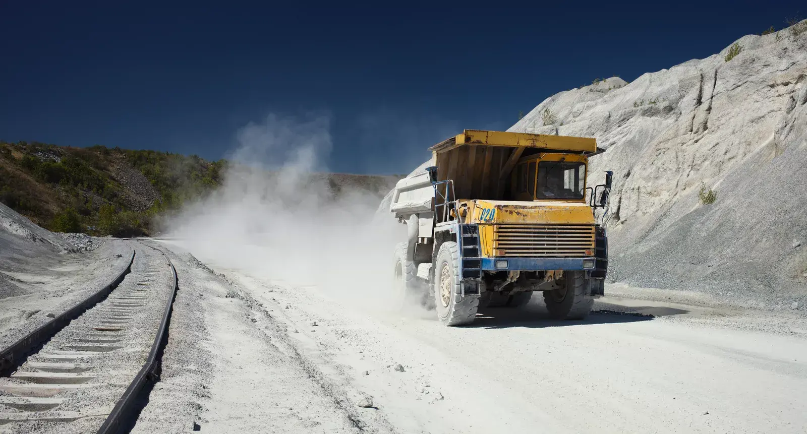 Dump truck operating on a dusty road demonstrating foam dust control system use to reduce airborne dust and protect machinery.