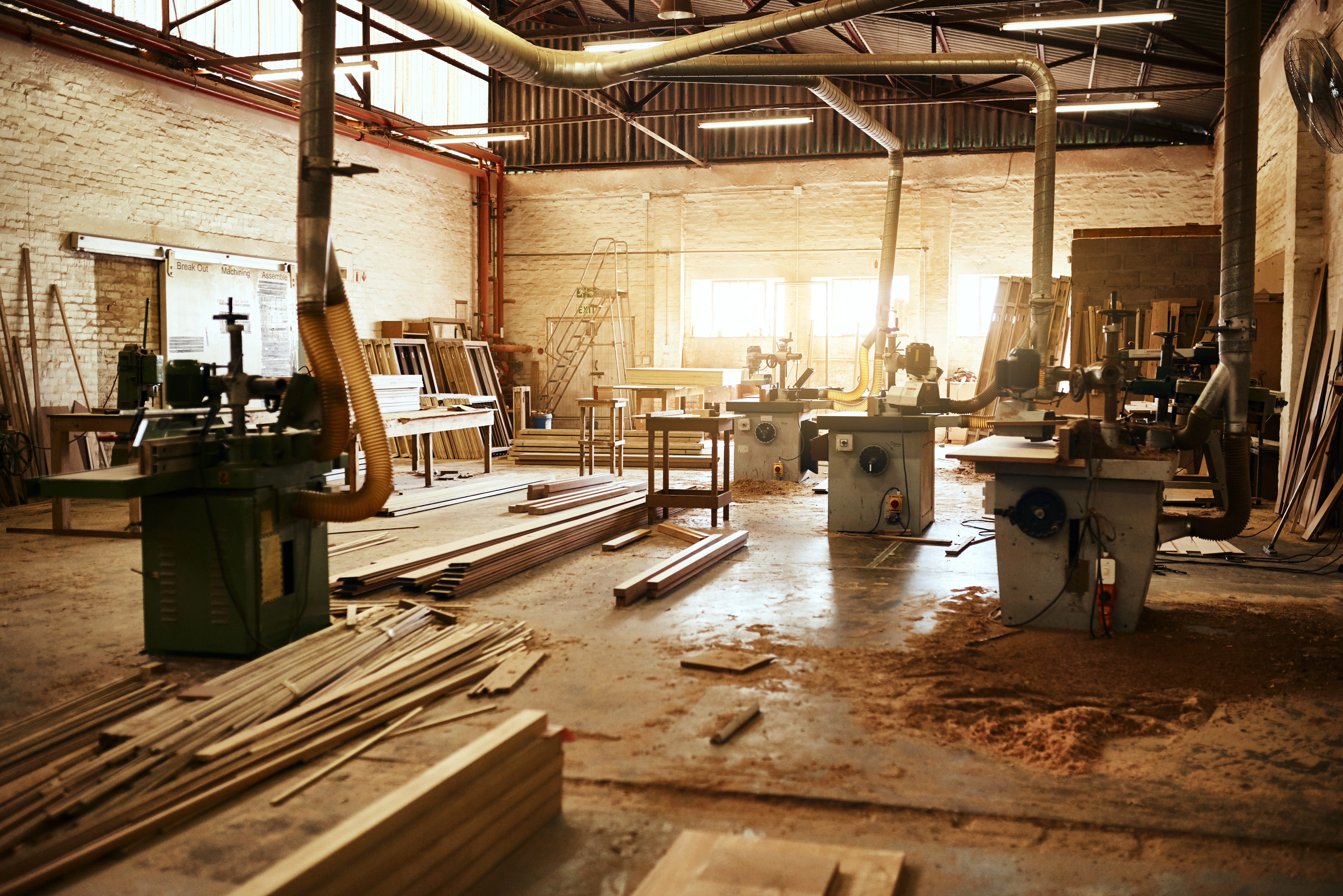 Timber workshop floor covered in wood shavings and sawdust with industrial machinery and dust extraction, highlighting the need for effective wood dust control measures.